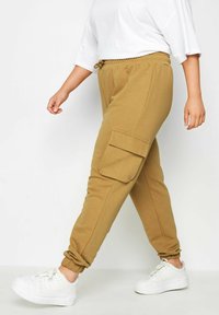 Bruna bomullsjoggers med manschetter vid anklarna, elastisk midja och sidfickor, kombinerat med vita sneakers.
