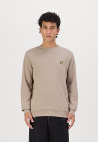 Beige színű pulóver, bordás kerek nyakkal és mandzsettákkal, a bal mellkasán egy kis sárga pillangólogóval. Sima textúrájú, laza fazon.