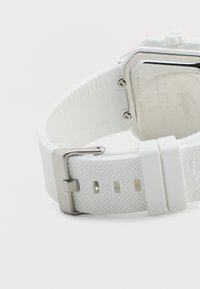 Λευκό ρολόι χειρός με λουράκι από υφασμένο σιλικόνη και αγκράφα από ανοξείδωτο ατσάλι, που δείχνει το χαραγμένο μεταλλικό πίσω μέρος της θήκης του ρολογιού.