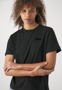 Melnas kokvilnas T-krekls ar īsām piedurknēm, ar maigu teksturētu logo kreisajā krūtī. Vienkārša apaļa kakla izgriezums un brīvs piegriezums.