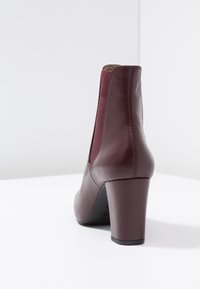 Maroon leather ankle boot with a square toe, elastic side panels, and a chunky heel. Smooth texture with subtle stitching details.