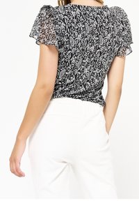 Černobílá květinová blůza s krátkými volánkovými rukávy, s vypasovaným pasem a lehkým texturovaným materiálem.
