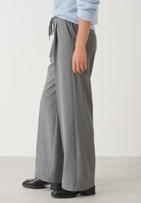 Gray wide-leg trousers featuring a drawstring waistband and textured fabric, paired with sleek black platform shoes.