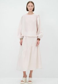 Outfit rosa chiaro composto da una blusa con maniche a palloncino e una gonna fluida con orlo arricciato. Il modello indossa sandali platform spessi.