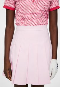 Rosa plisserad kjol tillverkad av ett mjukt material, kombinerad med en t-shirt med kort ärm som har ett geometriskt mönster i rosa och vitt.