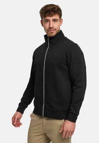 Svart zip-up sweatshirt med hög krage, smal passform, ribbade ärmslut och en logga på bröstet. Mjuk textur och minimalistisk design.