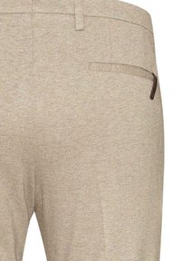 Béžové texturované kalhoty se zadní pravou kapsou s malým koženým akcentem na okraji kapsy.