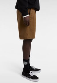 Bruine katoenen shorts met zijzakken, een rechte pasvorm en een nette zoom. Gecombineerd met zwarte sneakers en gestreepte zwarte sokken.