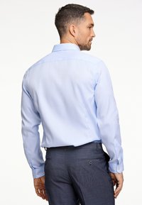Lichtblauw shirt met lange mouwen en een kraag met knopen, gladde textuur en contrasterende manchetten, gecombineerd met op maat gemaakte donkere broek.