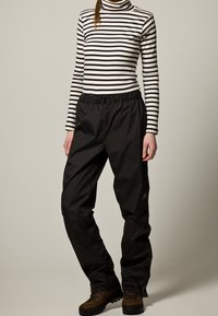 Černé nepromokavé kalhoty s elastickým pasem, nošené s černobílým pruhovaným rolákem. K outfitu doplňují hnědé turistické boty.