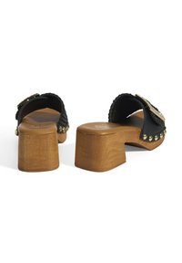 Zwarte open-teenslippers met een gestructureerde bovenkant, houten blokhak en decoratieve gouden studs langs de zool.