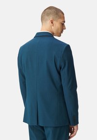 Giacca blu verde con un design strutturato, apertura centrale sul retro e due bottoni su ciascun polsino. Il tessuto sembra liscio con una vestibilità su misura.