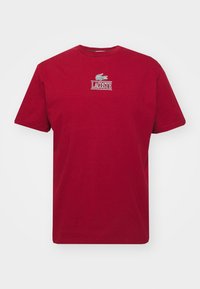 Röd bomulls-T-shirt med rund halsringning, korta ärmar och Lacoste-logotyp i vit och grön brodyr på bröstet.