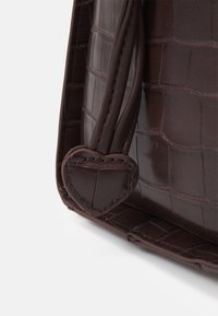 Brun krokodilprägling läderväska hörn med texturerad yta, slät sömnad och ett hjärtformat detalj på handtaget.