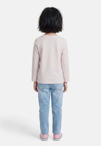 Παιδί με κοντά μαύρα μαλλιά φοράει ροζ ανοιχτόχρωμο μακρυμάνικο πουκάμισο, ανοιχτό μπλε τζιν και ροζ αθλητικά παπούτσια, στέκεται με την πλάτη προς τα έξω.