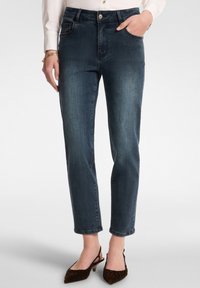 Tummansiniset farkut, joissa on korkea vyötärö, suora lahje, etutaskut ja vaaleaa kulutusta polvien läheisyydessä.