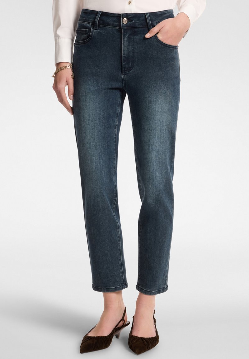 Tummansiniset farkut, joissa on korkea vyötärö, suora lahje, etutaskut ja vaaleaa kulutusta polvien läheisyydessä.