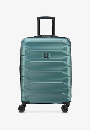 Valise rigide bleu sarcelle avec quatre roues noires, poignée télescopique déployée et logo circulaire au centre devant.