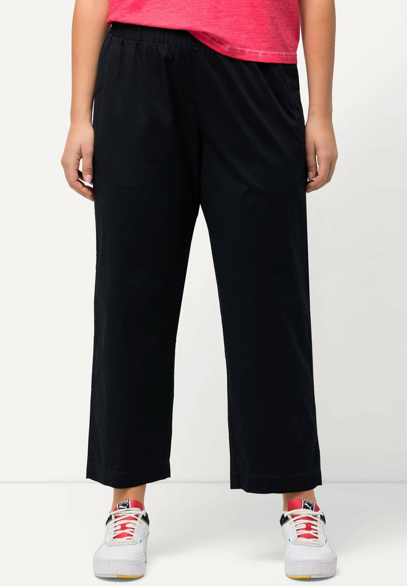 Pantaloni neri a culotte con fascia elastica in vita, caratterizzati da una texture liscia. Abbinati a sneakers bianche con accenti colorati.