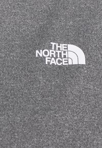 Wit "The North Face"-logo op gestructureerde grijze stof, gecentreerd met drie gebogen lijnen rechts van de tekst.