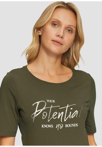 Olijfgroene t-shirt met korte mouwen en een ronde halslijn, voorzien van zilverkleurige metallic letters met de tekst "Je potentieel kent geen grenzen."