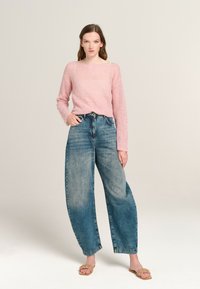 Helles rosa, gestricktes Sweatshirt mit langen Ärmeln, kombiniert mit hochgeschnittenen, weiten, ausgewaschenen blauen Jeans und beigen flachen Sandalen.