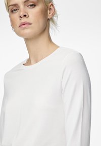 White long-sleeve shirt made of soft fabric with a round neckline. Features a smooth texture and fitted design, highlighting the collarbone area.
