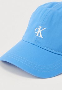 Ανοιχτό μπλε καπέλο τζόκεϊ από ύφασμα με ορατές ραφές. Διαθέτει λευκό κεντημένο λογότυπο 'cK' στο μπροστινό μέρος.