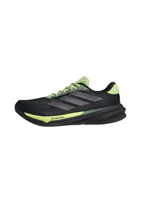 Zapatillas deportivas negras con acentos verdes, parte superior de malla y tres rayas grises. Cuenta con una suela curvada y un patrón de agarre texturizado.