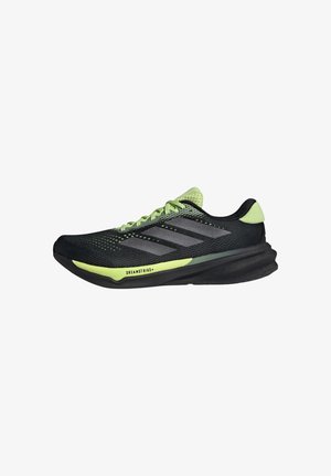 Chaussures de sport noires avec des accents verts, tige en maille et trois rayures grises. Présentent une semelle incurvée et un motif de grip texturé.