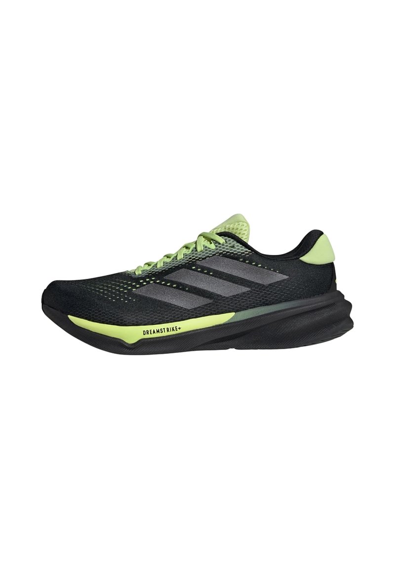 Zapatillas deportivas negras con acentos verdes, parte superior de malla y tres rayas grises. Cuenta con una suela curvada y un patrón de agarre texturizado.