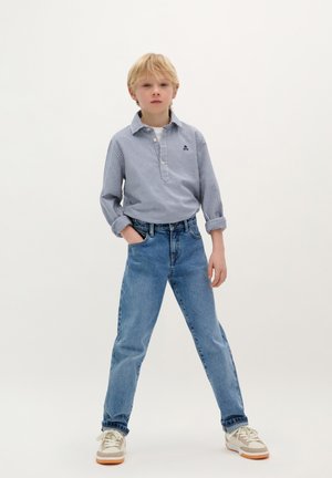 Camicia a quadri blu e bianca, maniche arrotolate, abbinata a jeans aderenti azzurri a vita alta e sneakers beige con accenti bianchi.