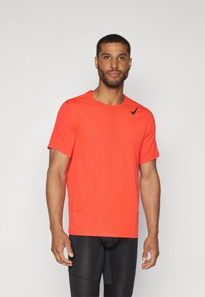 Pánské sportovní tričko jasně oranžové barvy s krátkým rukávem, texturovaná látka s malými perforacemi a černé logo Nike na hrudi.