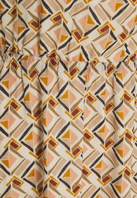 Mönstrad tyg med geometriska former i beige, orange, rosa och bruna nyanser, med en texturerad design som har veck längs midjan.