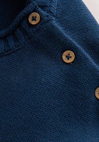 Marineblå strikket sweater med en tekstureret overflade, udstyret med en ribbet halsudskæring og fire runde, lyse knapper langs den ene skulder.