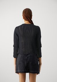 Maglione nero a maglia con motivi aperti, maniche a tre quarti e scollo rotondo, abbinato a una minigonna di jeans nera con orlo sfilacciato.