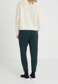 Suéter de punto crema con un patrón texturizado, combinado con pantalones oscuros de cuadros, ajustados, y zapatos negros sin cordones.