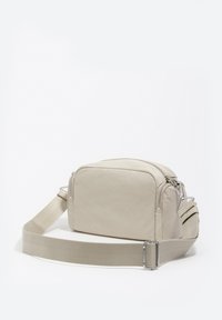 Beżowa torebka na ramię wykonana z gładkiej tkaniny, o prostokątnym kształcie, z dwoma zamkami błyskawicznymi, regulowanym paskiem i srebrną klamrą.