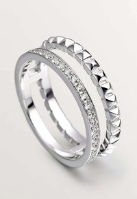 Anillos de plata apilados. Uno presenta una superficie lisa con piedras claras, el otro tiene un diseño con picos. Ambos están pulidos.