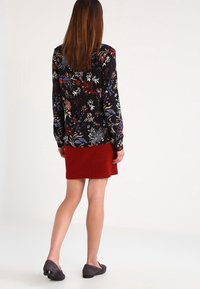 Blusa nera a fiori con maniche lunghe abbinata a una gonna rossa. La blusa presenta motivi floreali colorati; la gonna ha una texture morbida.
