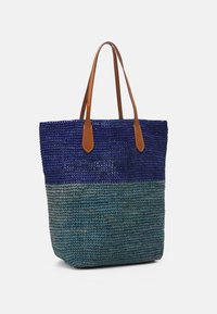 Vävd tote väska med marinblå och teal färgblockdesign, bruna syntetläderhandtag, öppen topp och texturerad yta.