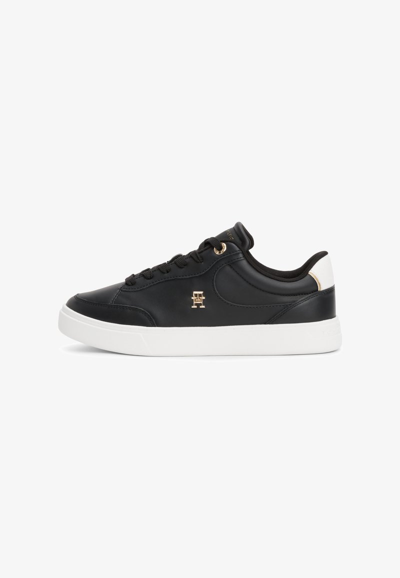 Sneaker in pelle nera con suola in gomma bianca, dotati di lacci neri, un emblema dorato e un accentuazione bianca a contrasto sul tallone.