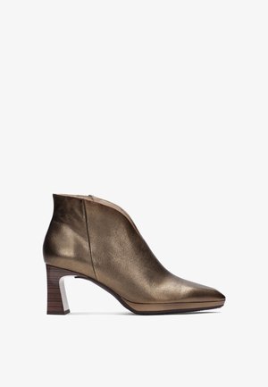 Botín de piel bronce con punta afilada, acabado texturizado y diseño de tacón medio. Presenta un cierre con cremallera y un acento de tacón de madera.