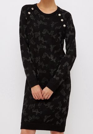 Robe en tricot noir avec un motif camouflage subtil, ornée de boutons argentés aux épaules et de poignets côtelés.
