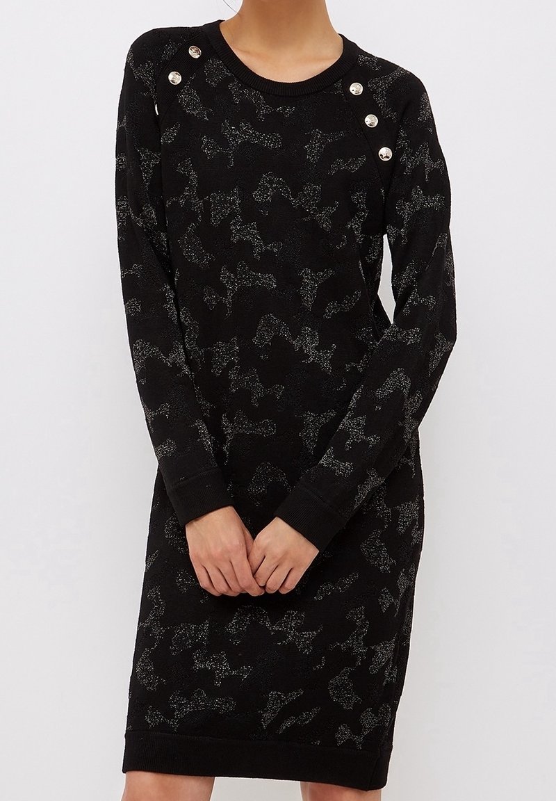Svart stickad klänning med ett subtilt kamouflage-mönster, prydd med silverfärgade knappar vid axlarna och ribbade ärmslut.