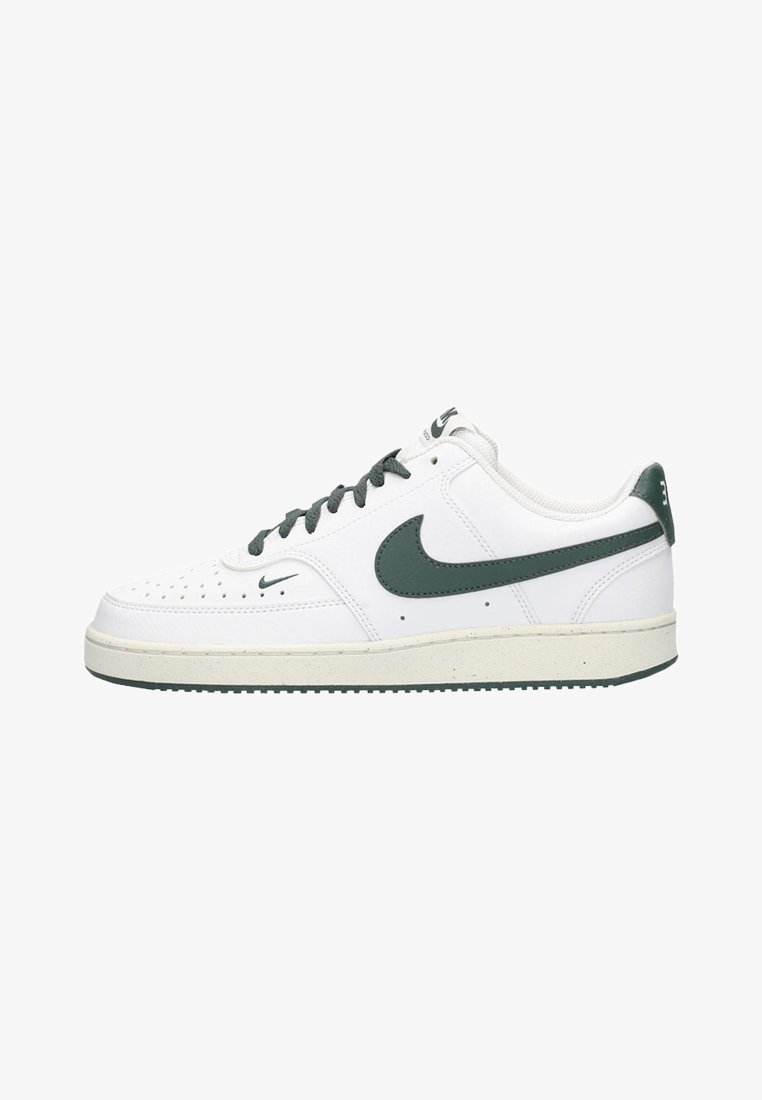 Zapatilla blanca con detalles verdes, parte superior de cuero texturizado, puntera perforada y cordones blancos. Presenta una suela de goma con un borde gris claro.