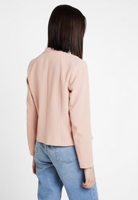 Jasnoróżowy blazer o strukturalnym kształcie, z długimi rękawami i krótką długością, wykonany z teksturowanej tkaniny, widok z tyłu.