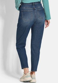 Jean taille haute bleu foncé au design ajusté, avec des poches arrière et une jambe fuselée. Associé à des baskets de sport de couleur claire.