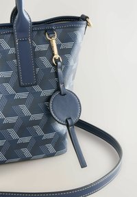 Navy handbag with geometric pattern. Features a circular tag with a strap, gold hardware accents, and textured leather finish.