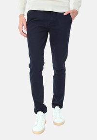 Chino blu navy in cotone, con un taglio slim, una texture sottile e tasche laterali, abbinati a sneakers bianche e un maglione leggero.
